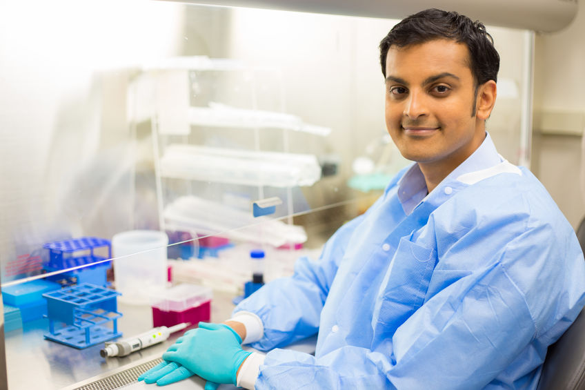 Scientist sitting in front of laboratory experiments and fume hood.