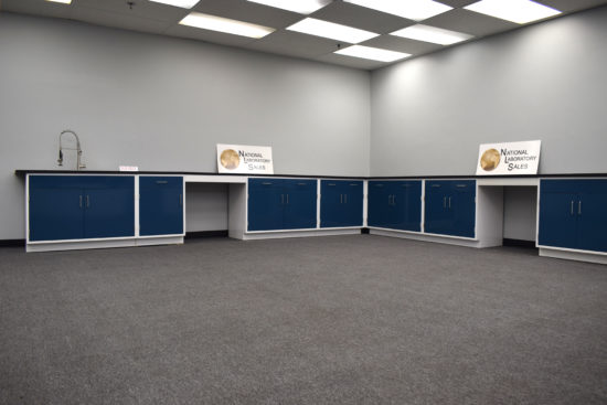 Blue laboratory cabinets with black countertops and two desks.