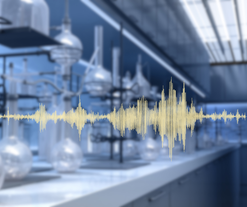 A laboratory with glassware such as flasks, beakers, and test tubes arranged on metal stands, illuminated by natural light from large windows. The background is intentionally blurred, emphasizing the central visual element: a waveform graphic representing sound waves, displayed in a yellowish hue.