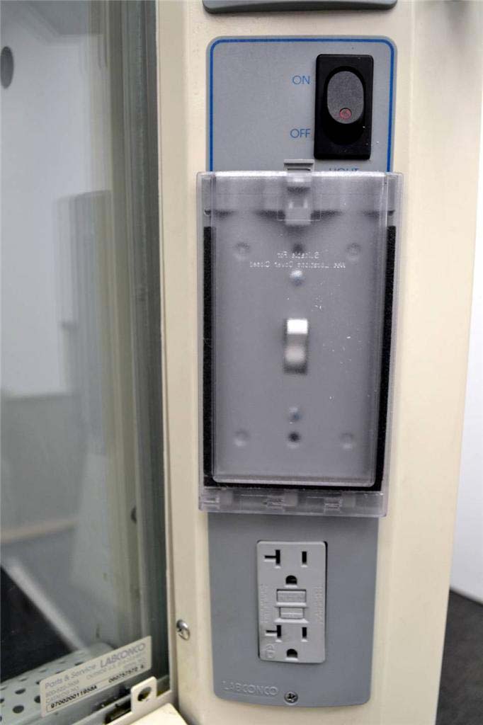 A close-up of the control panel on the exterior of a laboratory fume hood. At the top, there is a black on/off rocker switch labeled with "ON" and "OFF" in blue text. Below the switch, there is a covered panel with a transparent plastic cover, which is likely protecting additional controls or electrical components.